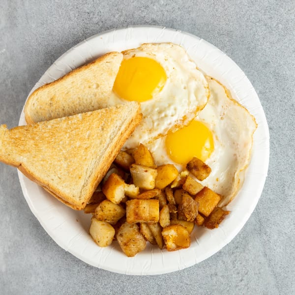 Breakfast plate with two fried eggs, golden-brown home fries, and two slices of toast.