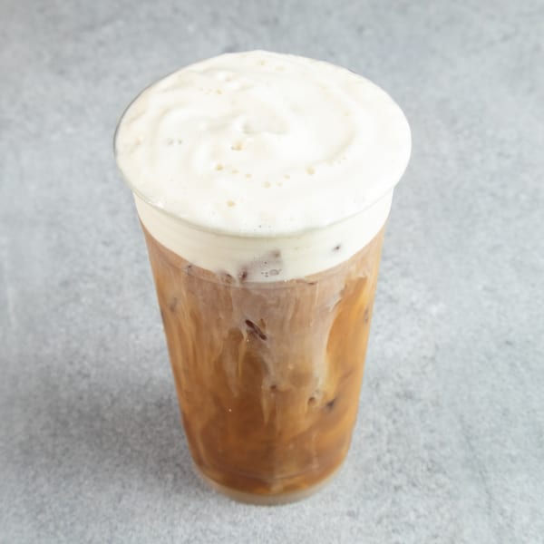 Iced coffee with a thick layer of white foam on top, in a clear plastic cup.
