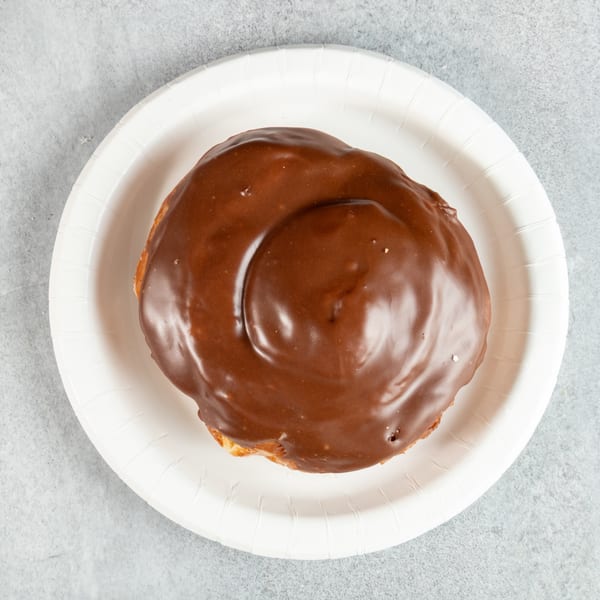Overhead view of a chocolate-glazed pastry on a white paper plate.