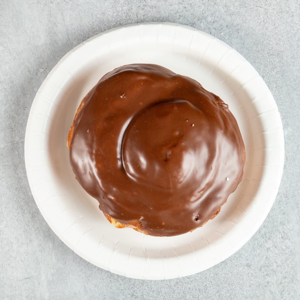 Overhead view of a chocolate-glazed pastry on a white paper plate.