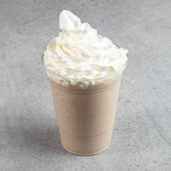 A chocolate milkshake in a clear plastic cup, topped with a generous swirl of white whipped cream.