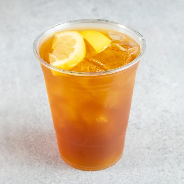 Iced tea with lemon slices and ice in a clear plastic cup on a gray surface.
