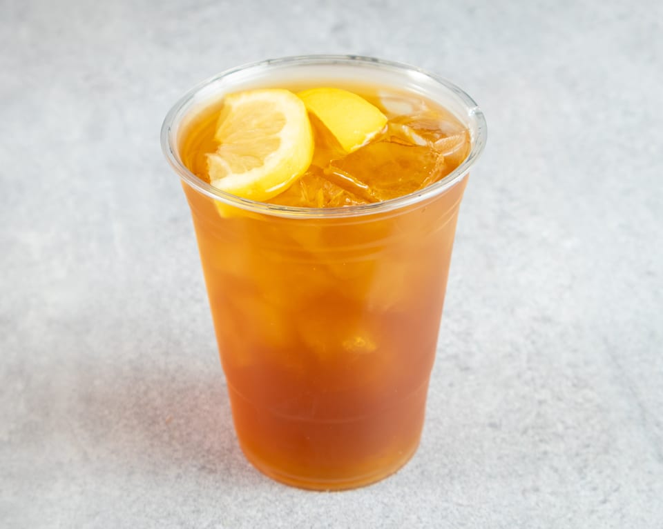 Iced tea with lemon slices and ice in a clear plastic cup on a gray surface.