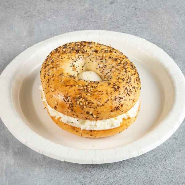 Everything bagel with cream cheese on a white paper plate.
