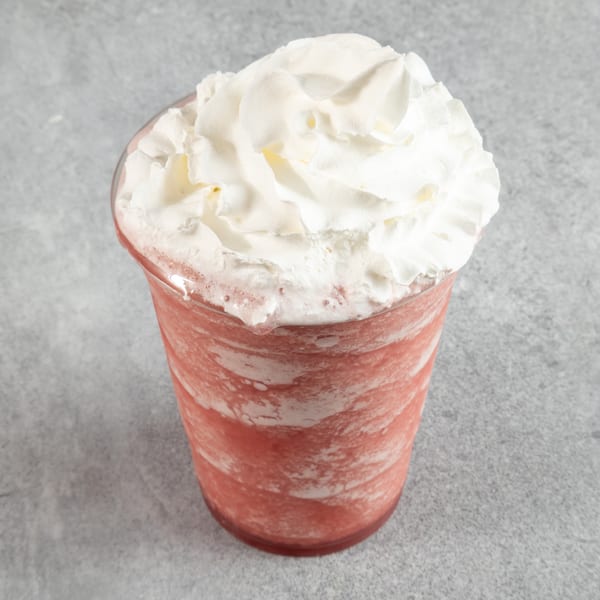 Pink frozen drink with whipped cream in a clear plastic cup on a gray surface.