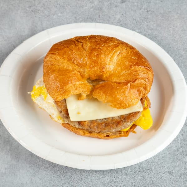 Croissant breakfast sandwich with sausage, egg, and cheese on a white paper plate.
