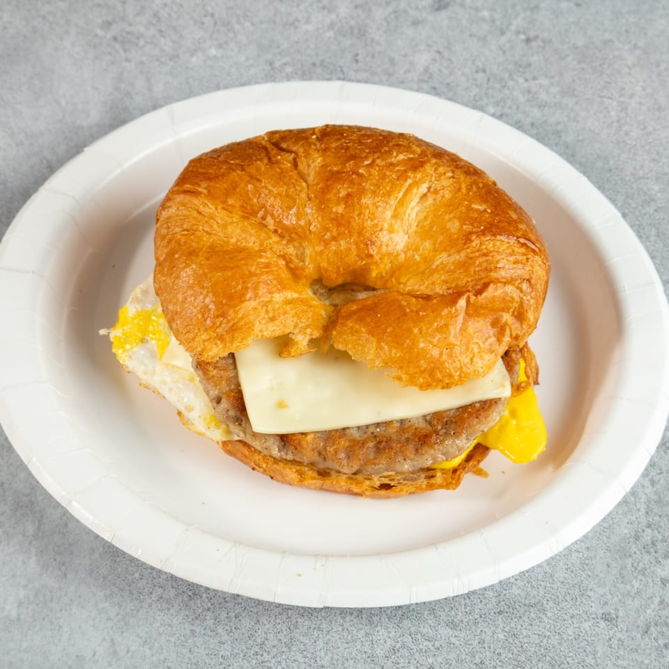 Croissant breakfast sandwich with sausage, egg, and cheese on a white paper plate.