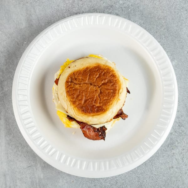 Breakfast sandwich with bacon, egg, and cheese on a toasted bun, served on a white plate.