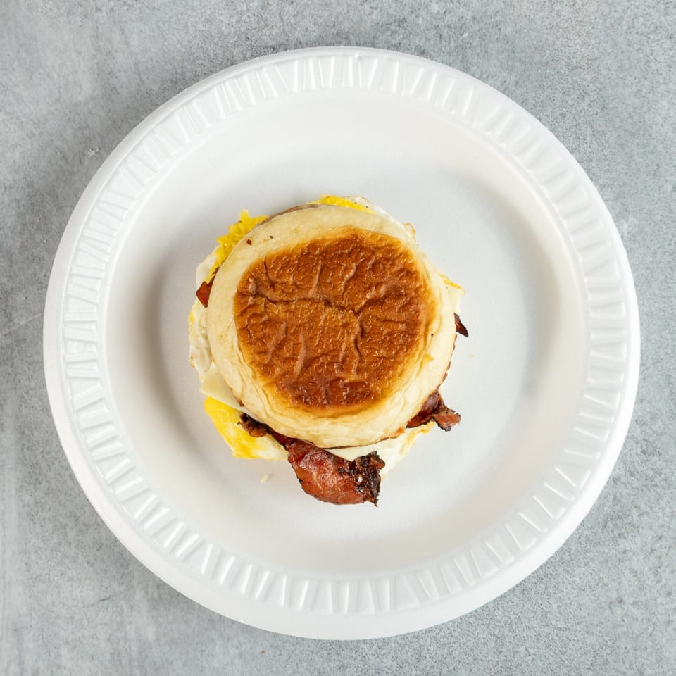 Breakfast sandwich with bacon, egg, and cheese on a toasted bun, served on a white plate.