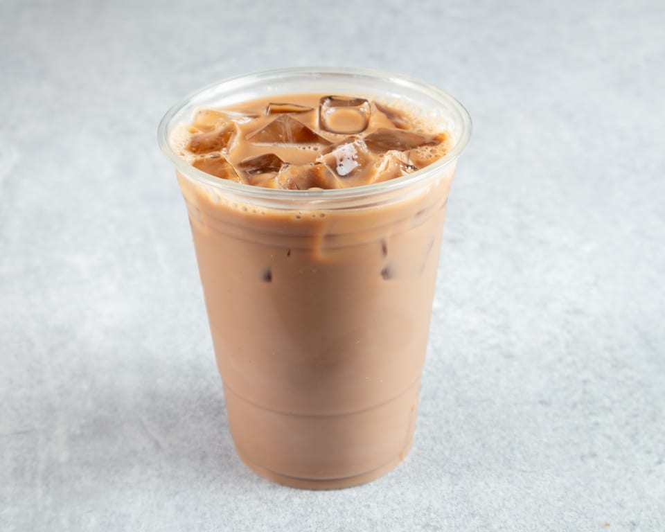 Iced coffee with milk and ice cubes in a clear plastic cup on a light gray surface.